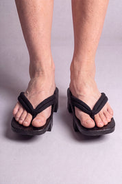Geta japonaise 'Tsushima' portée pieds nus, vue de face — lanière noire fine et souple sur plateforme surélevée en bois noirci