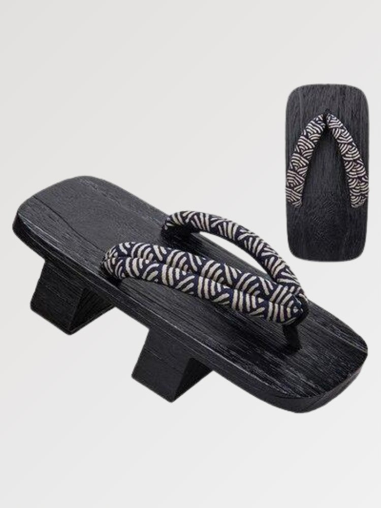 Paire de geta 'Shinshiro' vue de trois quarts — socle en bois noirci à deux dents, lanière à motif de vagues noir et blanc, dessous visible