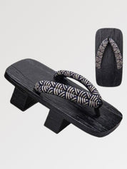 Paire de geta 'Shinshiro' vue de trois quarts — socle en bois noirci à deux dents, lanière à motif de vagues noir et blanc, dessous visible
