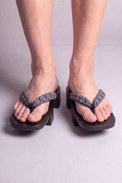 Geta japonaise 'Shinshiro' portée pieds nus, vue de face — lanière à motif de vagues noir et blanc sur plateforme surélevée en bois noirci