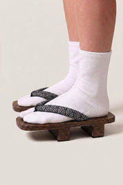 Geta japonaise 'Seigaiha' portée avec des chaussettes tabi blanches, vue de profil — plateforme en bois foncé, lanière à motif de vagues seigaiha noir et blanc