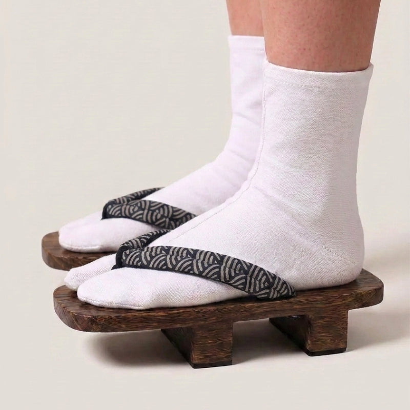 Geta japonaise 'Seigaiha' portée avec des chaussettes tabi blanches, vue de profil — plateforme en bois foncé, lanière à motif de vagues seigaiha noir et blanc