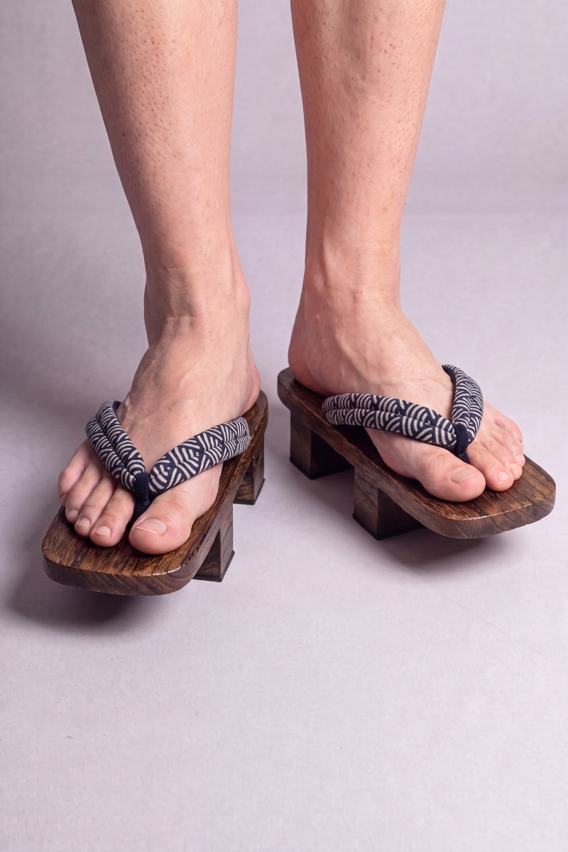Geta japonaise 'Seigaiha' portée pieds nus, vue de face — lanière à motif de vagues seigaiha noir et blanc sur plateforme surélevée en bois foncé