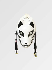 Masque de chat noir et blanc présenté de face sur fond gris uni — félin blanc aux larges aplats noirs autour des yeux, pompons noirs et grelots