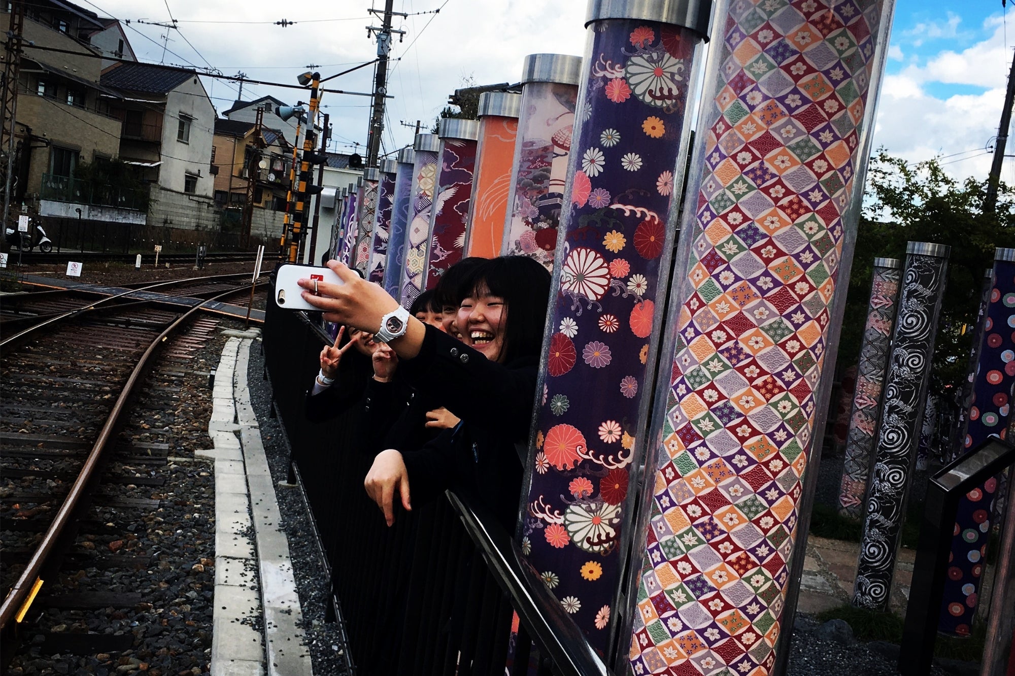 Groupe de lycéennes japonaises souriantes prenant un selfie parmi les colonnes lumineuses d’Arashiyama à Kyoto, symbole du Japon moderne et coloré.