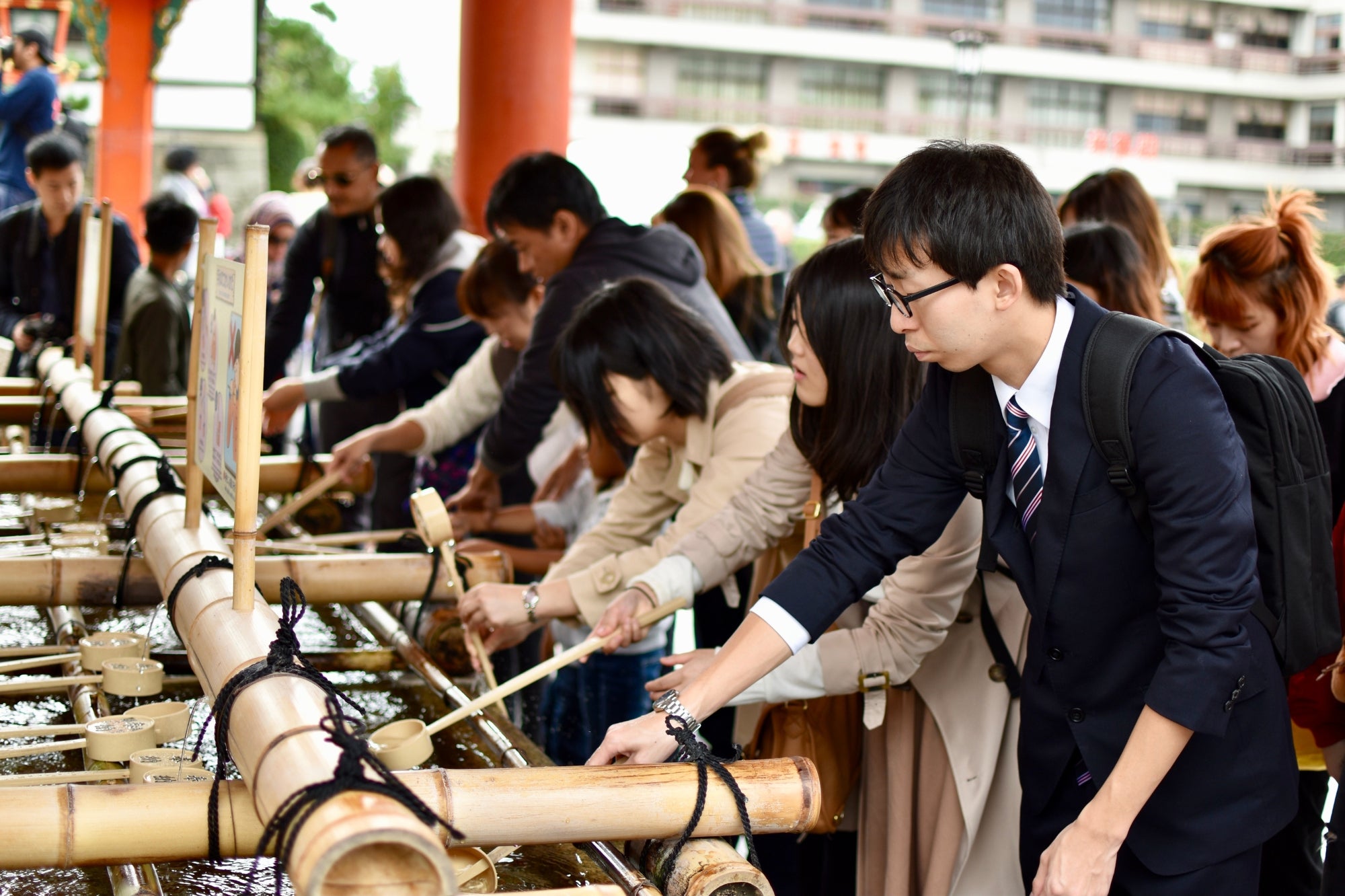 Des visiteurs japonais effectuent un rituel de purification à l’eau dans un temple de Kyoto, symbole des traditions spirituelles du Japon.