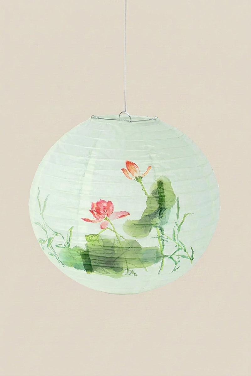 Lanterne japonaise coloris fleur de lotus — lanterne boule en papier vert d'eau ornée d'un lotus rose et de feuillages, suspendue à un fil sur fond beige uni