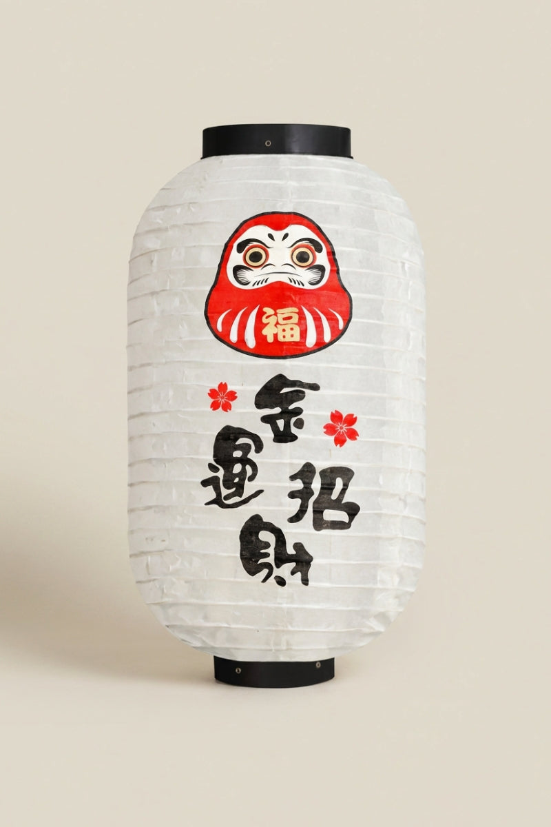 Lanterne japonaise — lanterne cylindrique en papier blanc à daruma rouge et calligraphie noire, cerclages noirs en haut et en bas, photo sur fond beige