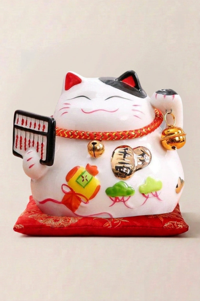 Maneki neko tirelire 'Lucky Abacus' en céramique — chat blanc tenant un boulier noir, motifs floraux sur le ventre et grelots, sur un coussin rouge