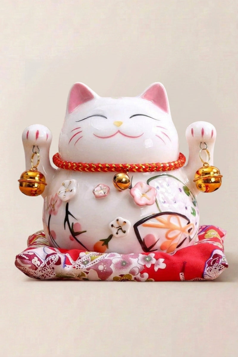 Maneki neko tirelire 'Tinkerbell' en céramique — chat blanc couvert de grelots dorés et de fleurs, les deux pattes levées, sur un coussin rouge