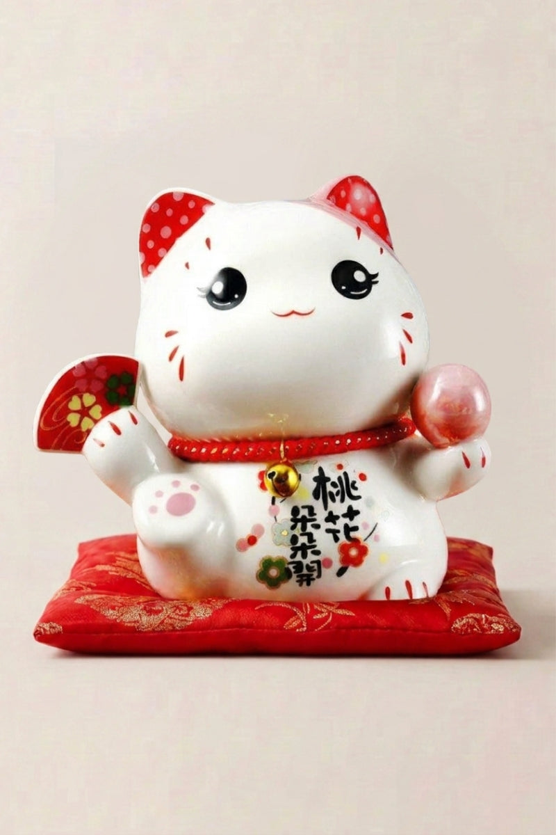 Maneki neko tirelire 'Love' en céramique — chat blanc à motifs floraux tenant une plaque rouge, patte droite levée, sur un coussin rouge