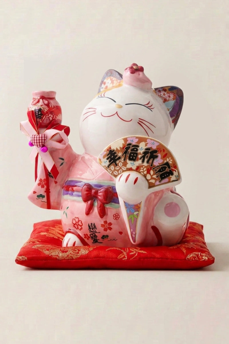 Maneki neko tirelire 'Pink Fortune' en céramique — chat rose semé de fleurs et d'éventails, patte droite levée, grand format, sur un coussin rouge