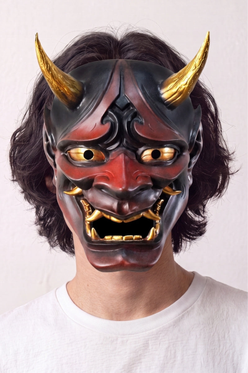 Masque hannya rouge porté par un mannequin sur fond clair — démon rouge et noir aux cornes dorées, crocs blancs et regard cerné d'or