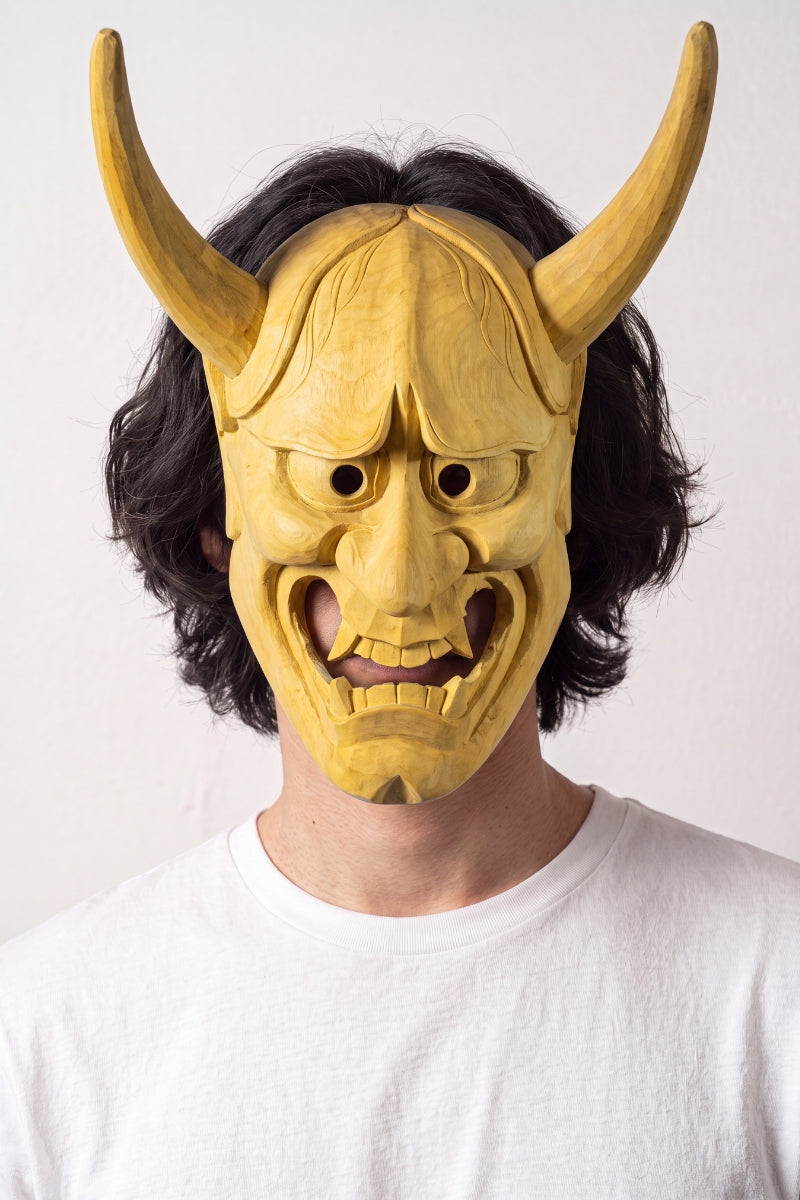 Masque oni en bois clair porté par un mannequin sur fond clair — démon aux deux longues cornes recourbées, visage allongé et bouche entrouverte