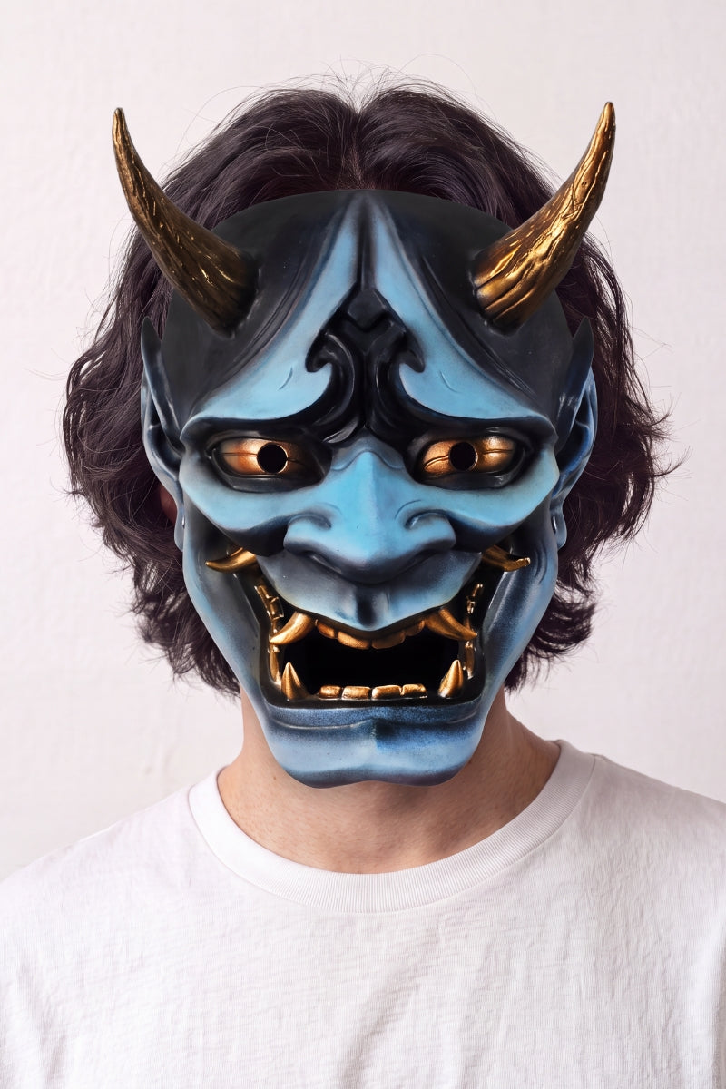 Masque hannya bleu porté par un mannequin sur fond clair — démon bleu aux cornes dorées, sourcils froncés et bouche ouverte sur des crocs