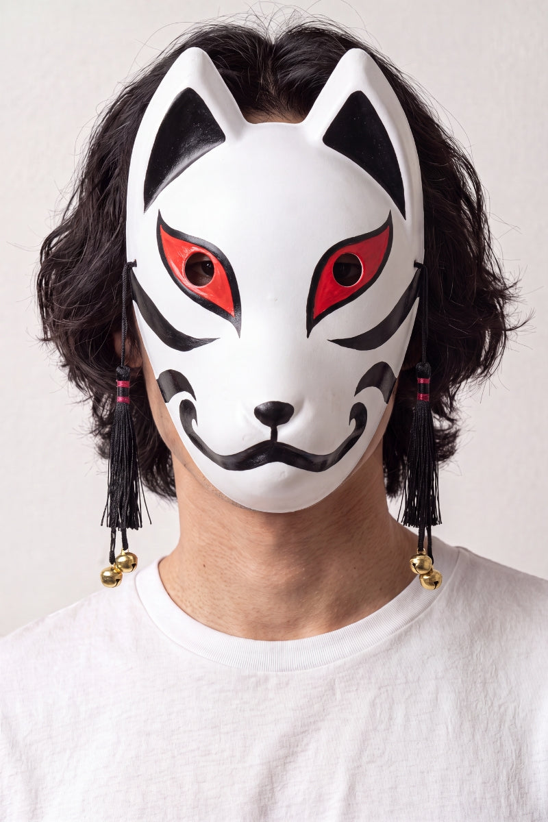 Masque kitsune noir et blanc porté par un mannequin sur fond clair — renard blanc à oreilles et contours noirs, museau rouge et pompons noirs