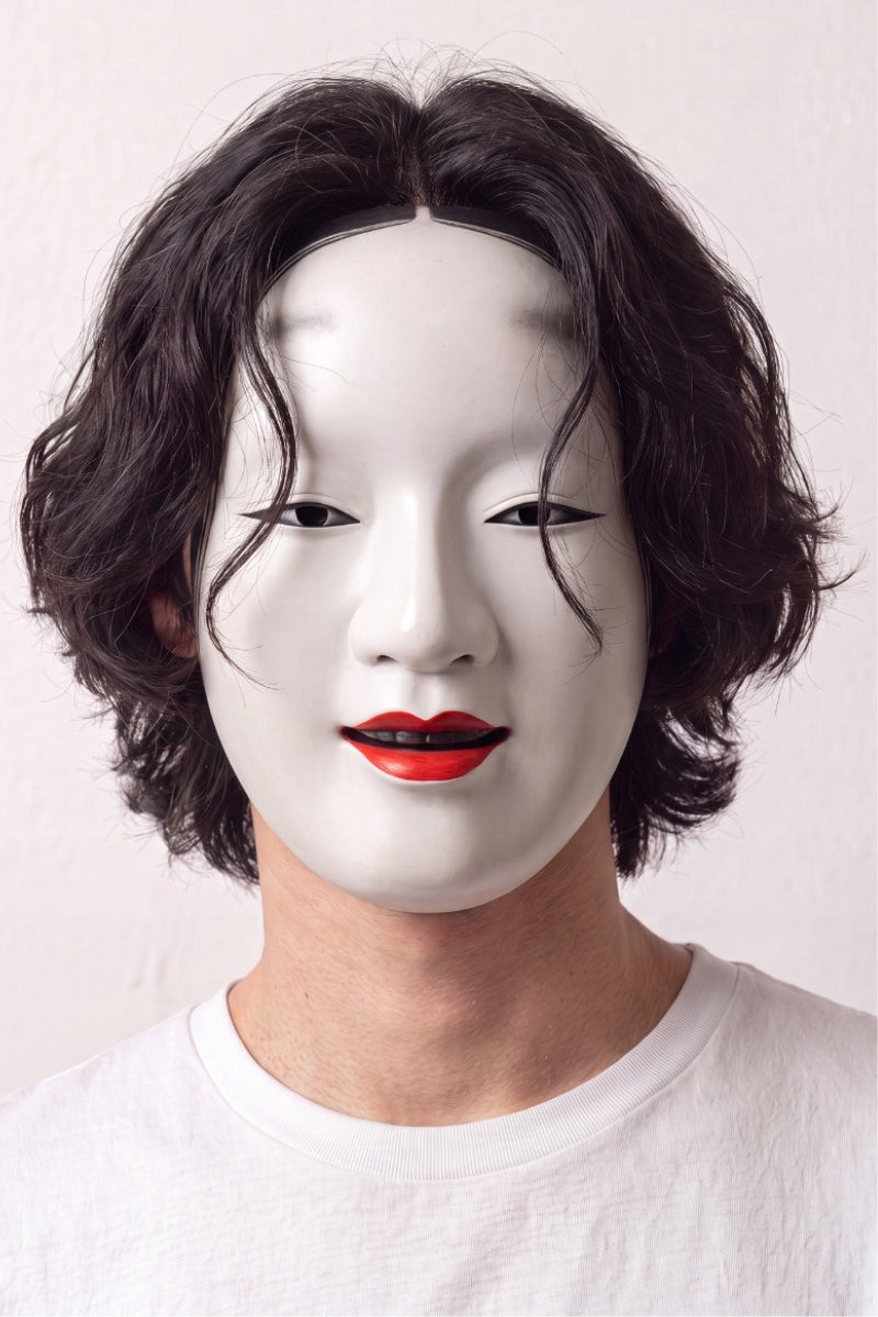 Masque de nô porté par un mannequin sur fond clair — visage féminin blanc laqué, lèvres rouges et sourcils hauts peints