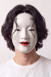 Masque de nô porté par un mannequin sur fond clair — visage féminin blanc laqué, lèvres rouges et sourcils hauts peints