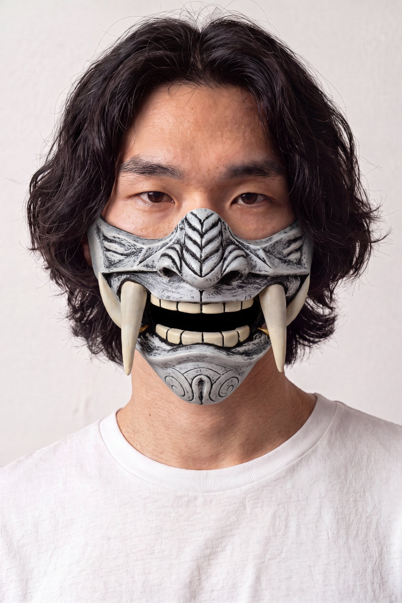 Demi-masque mempō argenté porté par un mannequin sur fond clair — protection gris argent gravée de motifs en relief, dents apparentes et crocs