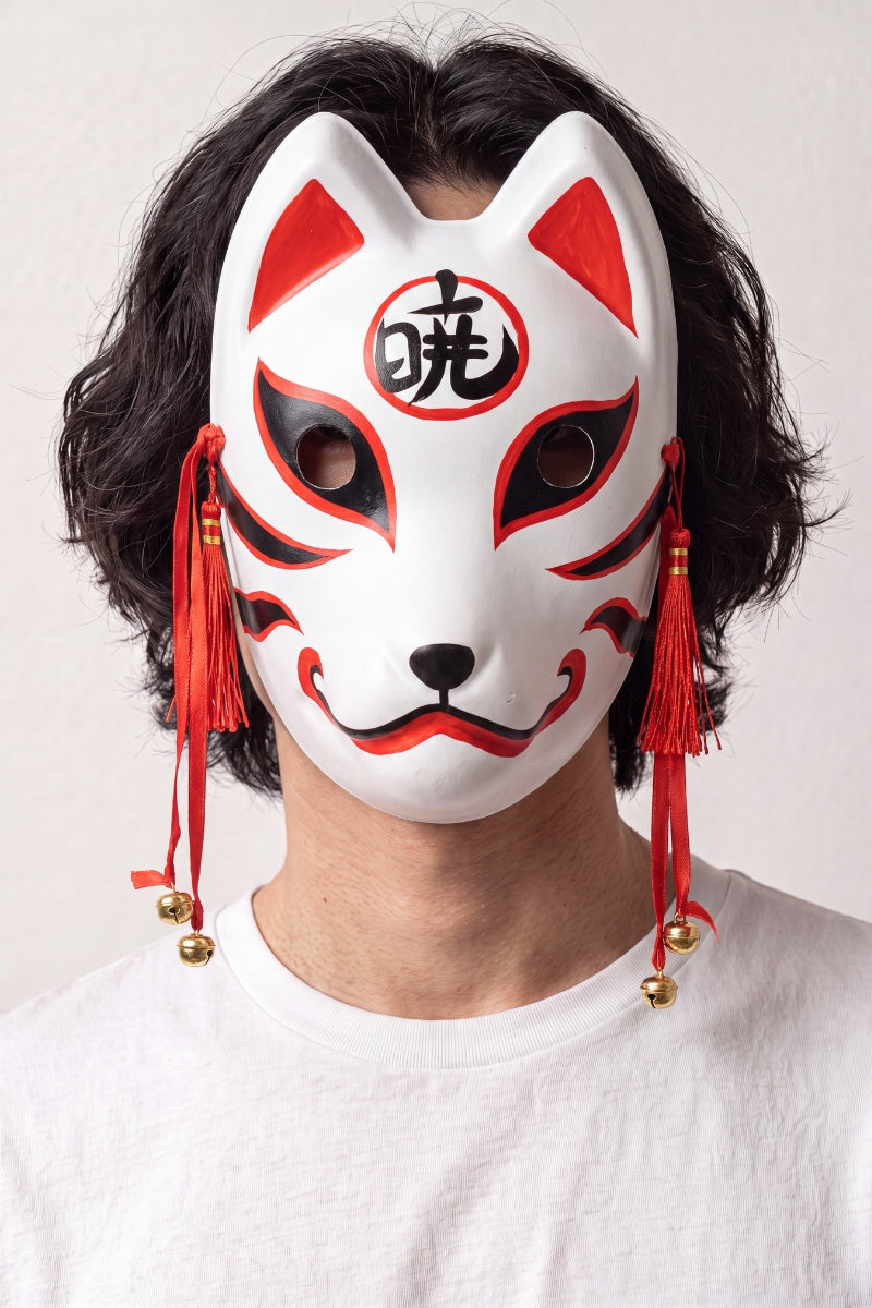 Masque kitsune au kanji porté par un mannequin sur fond clair — renard blanc portant un kanji rouge au front, cordons et grelots dorés
