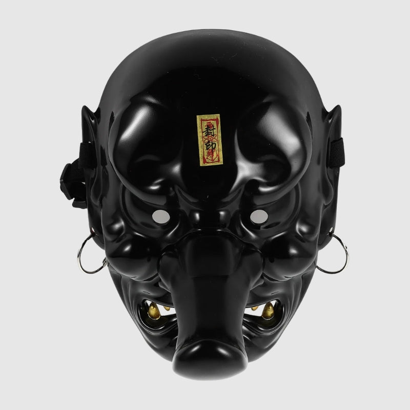 Masque tengu noir présenté de face sur fond gris uni — long nez proéminent, sourcils en volutes dorées et crocs blancs