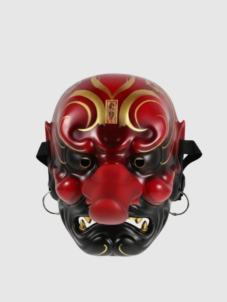 Masque tengu rouge présenté de face sur fond gris uni — long nez proéminent, sourcils en volutes dorées et crocs blancs