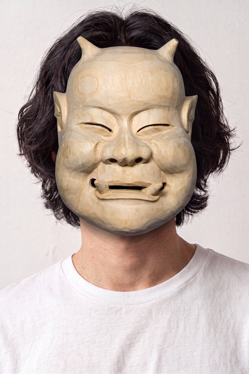 Masque de nô beige porté par un mannequin sur fond clair — visage âgé souriant aux yeux plissés, teinte sable et modelé sobre