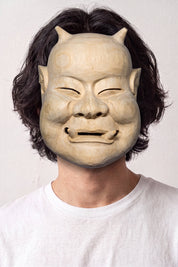 Masque de nô beige porté par un mannequin sur fond clair — visage âgé souriant aux yeux plissés, teinte sable et modelé sobre