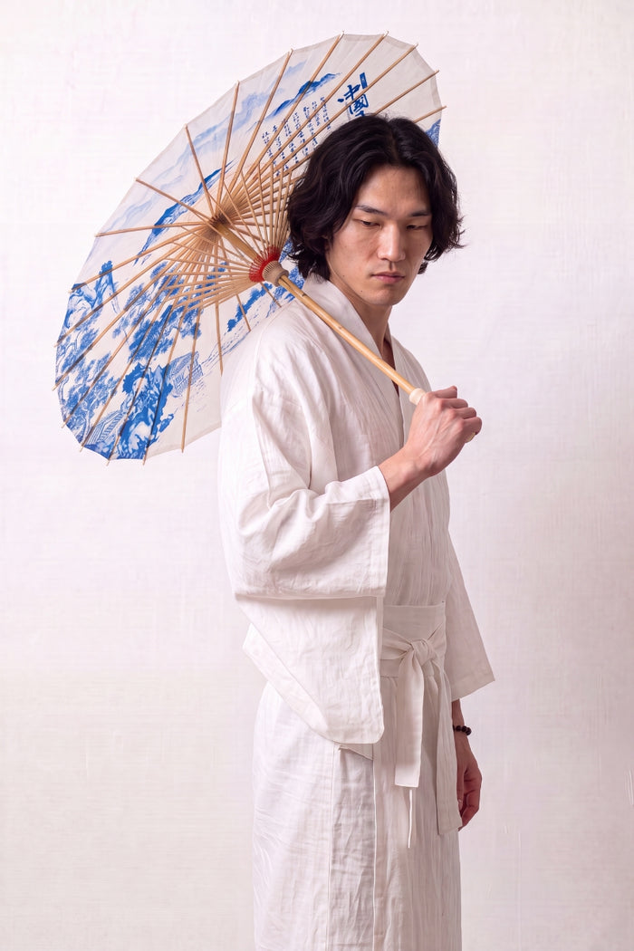 Ombrelle japonaise 'Kashika' ouverte et tenue par un mannequin en kimono blanc — toile blanche à motif de jardin bleu, feuillages et pavillons