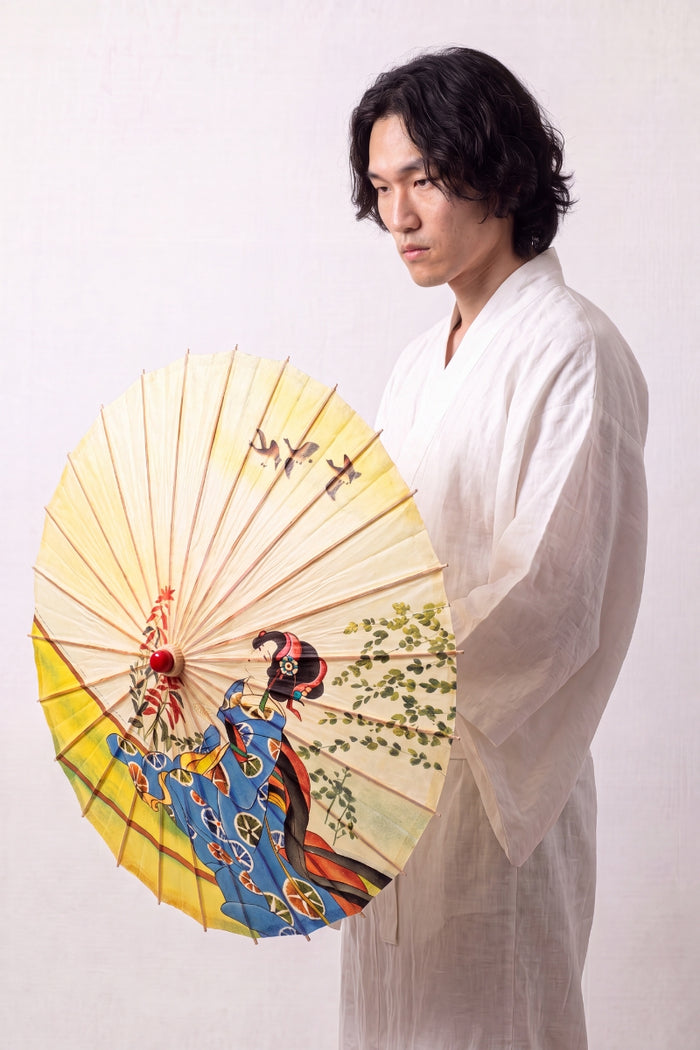 Ombrelle japonaise 'Shojino' ouverte et tenue par un mannequin en kimono blanc — toile jaune et bleue à figure de maiko et branches fleuries