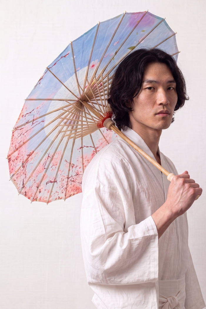 Ombrelle japonaise 'Kekkon' ouverte et tenue par un mannequin en kimono blanc — toile bleu clair et rose à nuages stylisés et fleurs