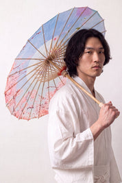 Ombrelle japonaise 'Kekkon' ouverte et tenue par un mannequin en kimono blanc — toile bleu clair et rose à nuages stylisés et fleurs