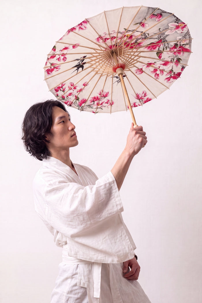 Ombrelle japonaise 'Nomikomu' ouverte et tenue par un mannequin en kimono blanc — toile crème couverte de fleurs de cerisier roses