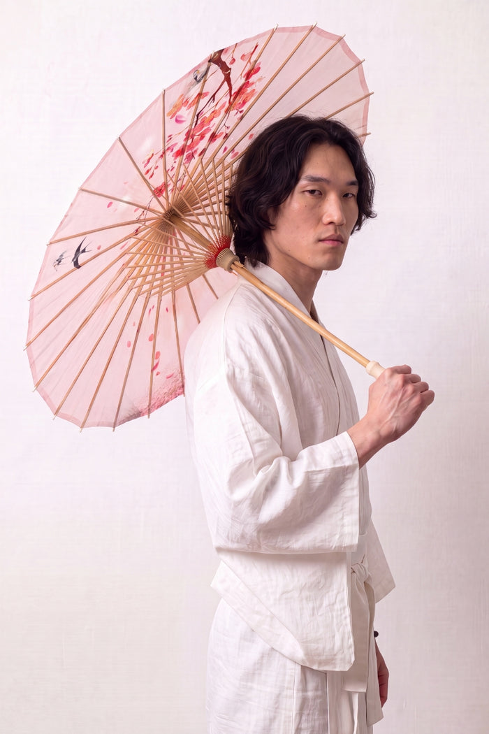 Ombrelle japonaise 'Sakura Classic' ouverte et tenue par un mannequin en kimono blanc — toile rose pâle à oiseaux et fines branches fleuries