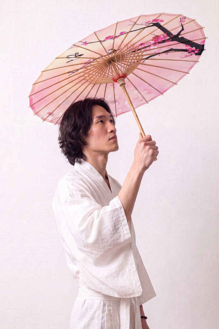 Ombrelle japonaise 'Sakura Fleuri' ouverte et tenue par un mannequin en kimono blanc — toile rose dégradée à branche sombre et fleurs de cerisier