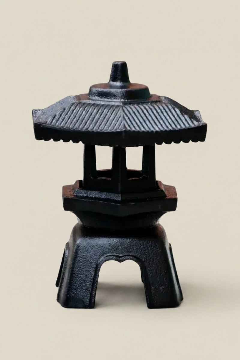 Lanterne japonaise — petite lanterne en fonte noire à toit hexagonal nervuré et corps ouvert sur quatre montants, photo produit sur fond beige uni