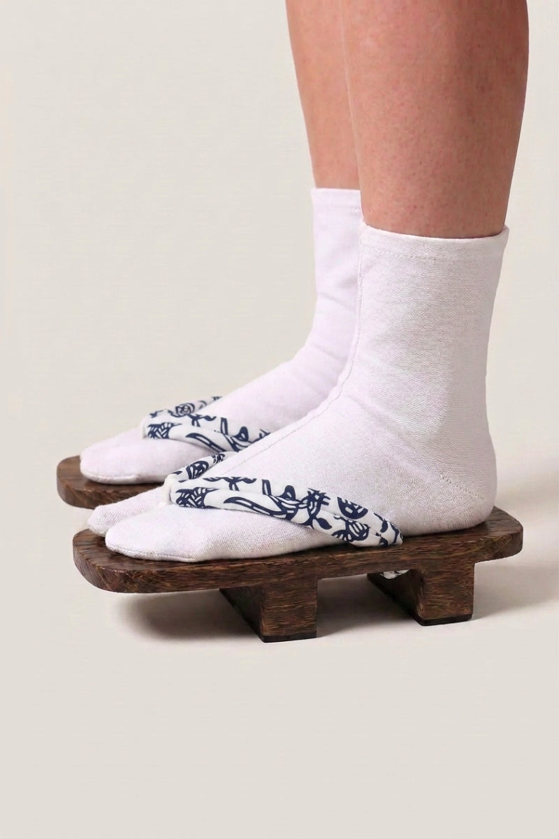 Geta japonaise 'Okayama' portée avec des chaussettes tabi blanches, vue de profil — plateforme en bois brun, lanière blanche à motif floral bleu nuit