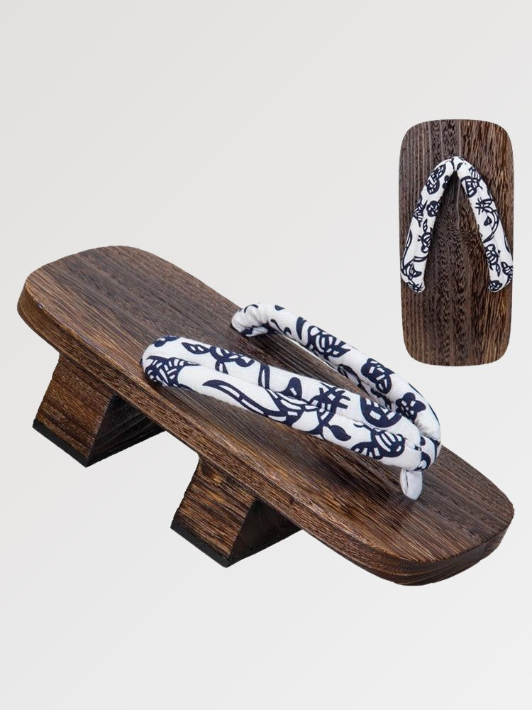 Paire de geta 'Okayama' vue de trois quarts — socle en bois brun à deux dents, lanière blanche à motif floral bleu nuit, dessous visible