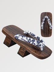 Paire de geta 'Okayama' vue de trois quarts — socle en bois brun à deux dents, lanière blanche à motif floral bleu nuit, dessous visible