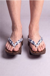 Geta japonaise 'Okayama' portée pieds nus, vue de face — lanière blanche à motif floral bleu nuit sur plateforme surélevée en bois brun