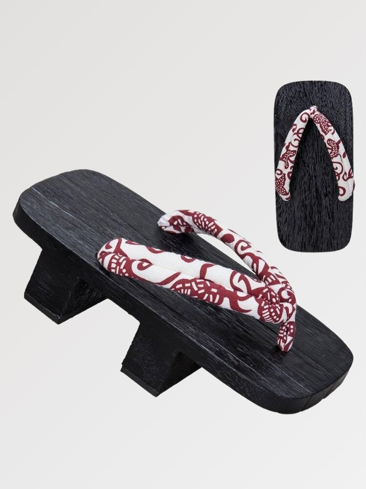 Paire de geta 'Aomori' vue de trois quarts — socle en bois noirci à deux dents, lanière rouge et blanche à motif cachemire, dessous visible