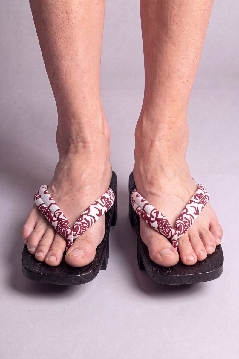 Geta japonaise 'Aomori' portée pieds nus, vue de face — lanière rouge et blanche à motif cachemire sur plateforme surélevée en bois noirci