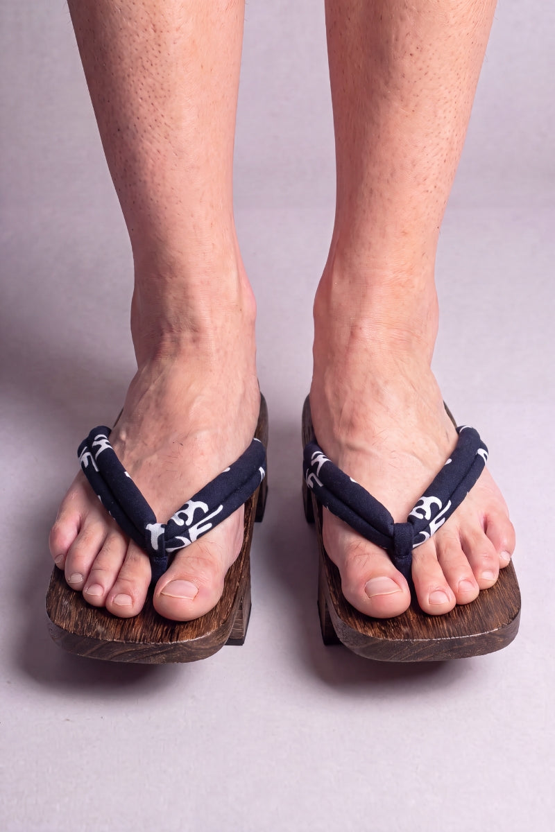 Geta japonaise 'Kurashiki' portée pieds nus, vue de face — lanière bleu nuit à motif blanc sur plateforme surélevée en bois foncé