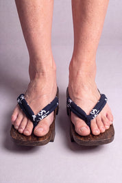 Geta japonaise 'Kurashiki' portée pieds nus, vue de face — lanière bleu nuit à motif blanc sur plateforme surélevée en bois foncé