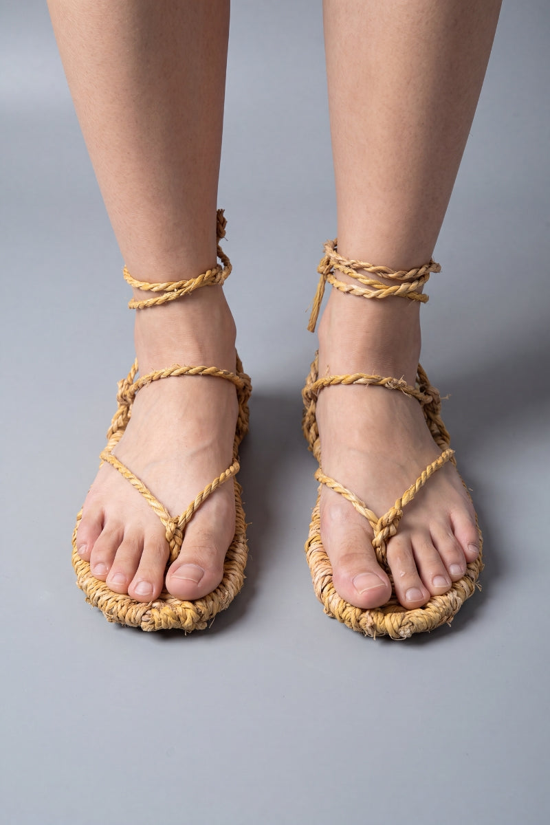 Sandales waraji portées pieds nus, vue de face : semelles en paille tressée et cordes croisées sur le cou-de-pied