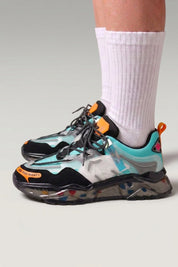 Baskets chunky 'Hekinan' coloris bleu — semelle translucide parsemée d'éclats multicolores, portées avec chaussettes blanches sur fond studio gris