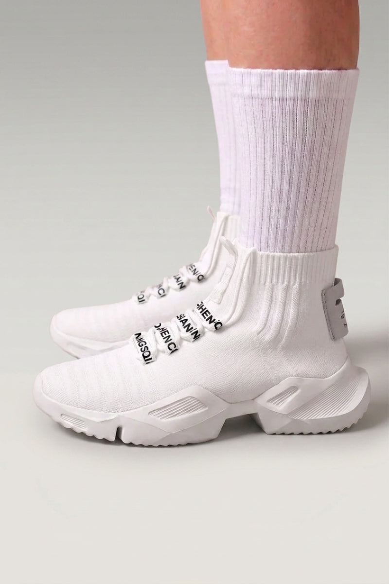 Baskets montantes 'Kashiwa' coloris blanc — maille tricotée montante sans lacets, semelle épaisse, portées avec chaussettes blanches sur fond studio gris