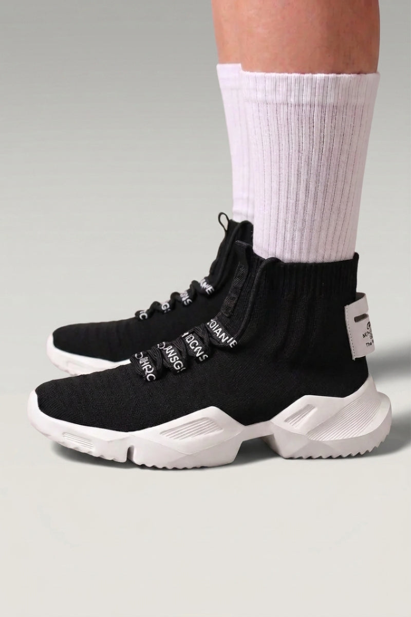 Baskets montantes 'Kashiwa' coloris noir — maille tricotée montante sans lacets, semelle épaisse, portées avec chaussettes blanches sur fond studio gris