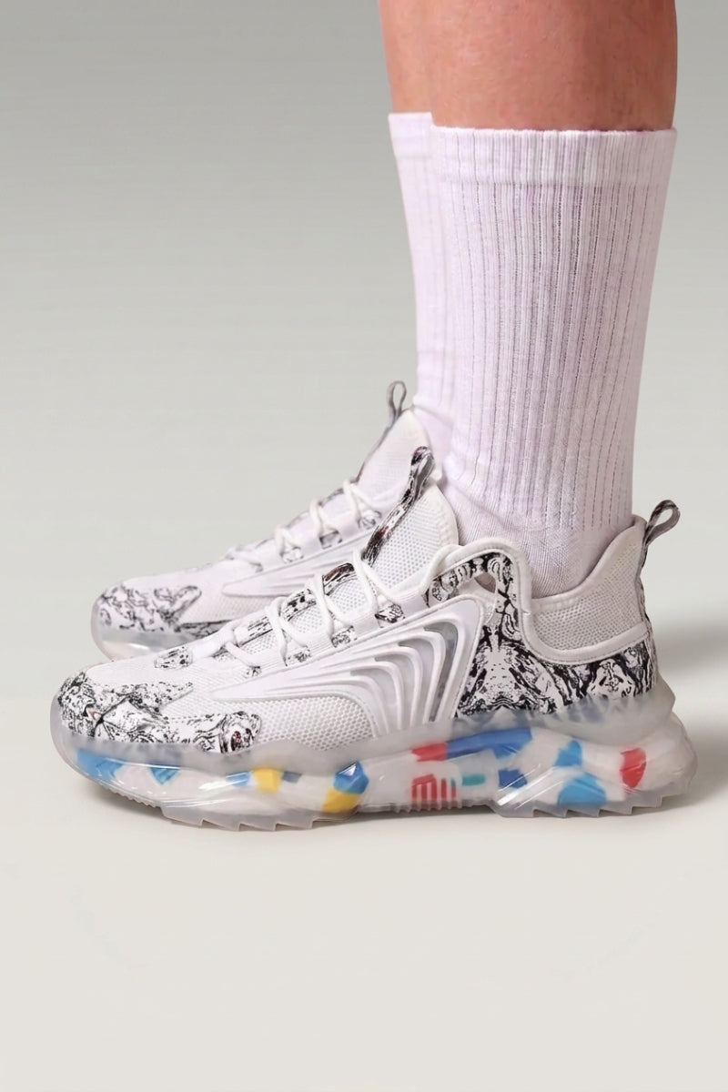 Baskets chunky 'Kariya' coloris blanc — imprimé tribal intégral, semelle translucide à confettis, portées avec chaussettes blanches sur fond studio gris