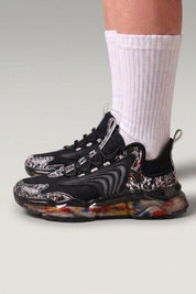 Baskets chunky 'Kariya' coloris noir — imprimé tribal intégral, semelle translucide à confettis, portées avec chaussettes blanches sur fond studio gris
